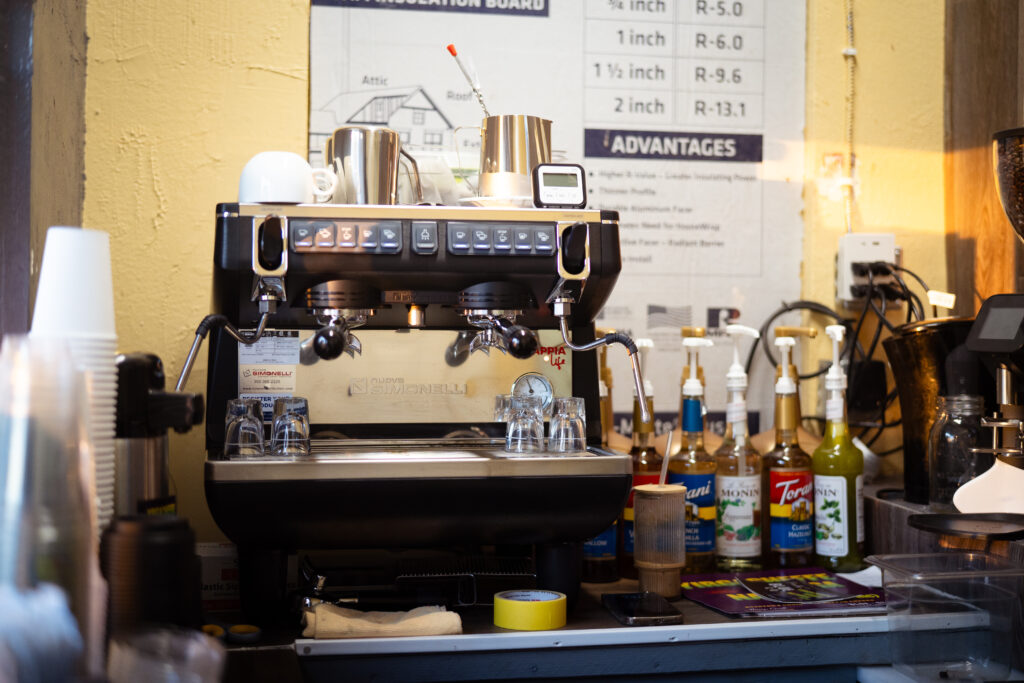 A silver coffee machine photographed inside with different syrup options on a shelf