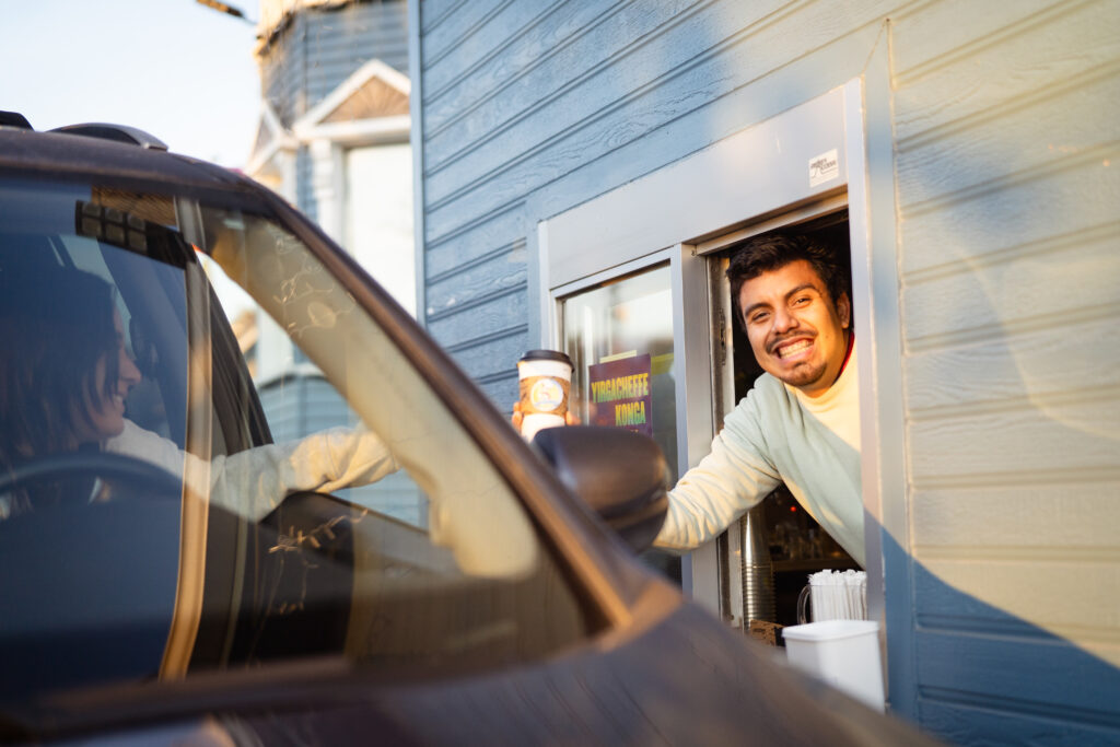 A smiling drive-thru employee handing a coffee order to a customer