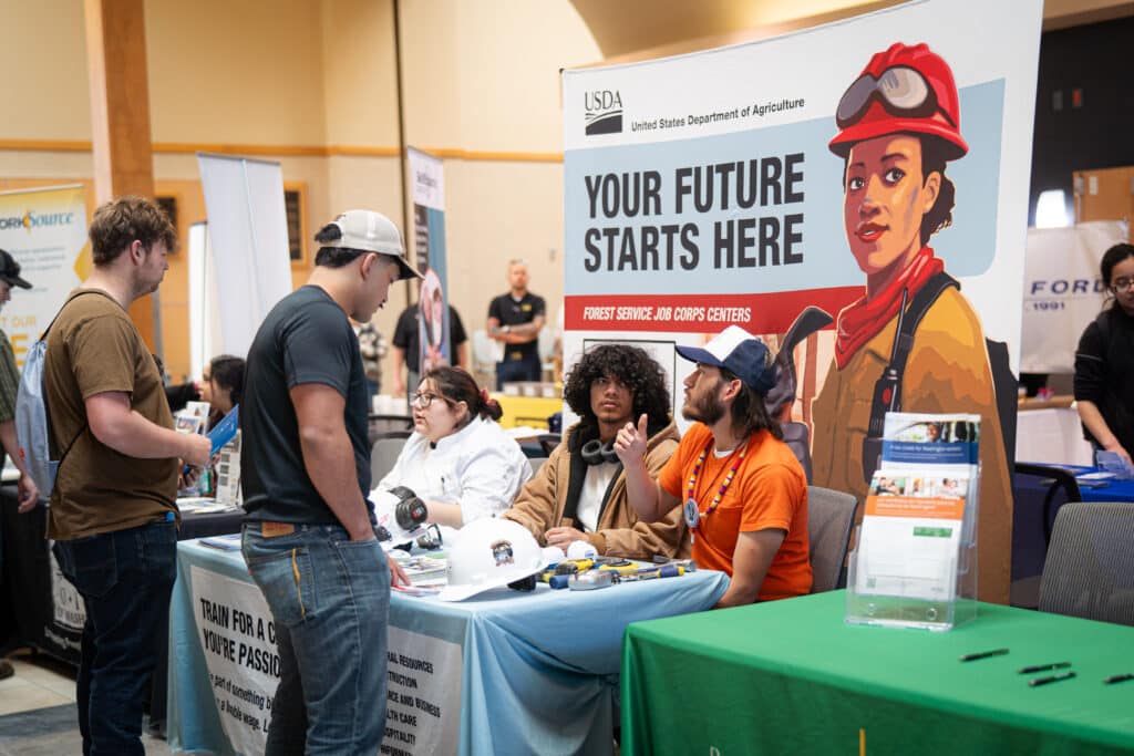 A group of 3 individuals explaining their services to two males at the job fair at Big Bend Community College