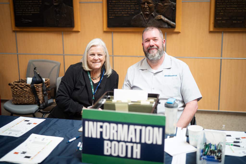 Two adults sitting at a table smiling at the camera at the Big Bend Community College's Job Fair