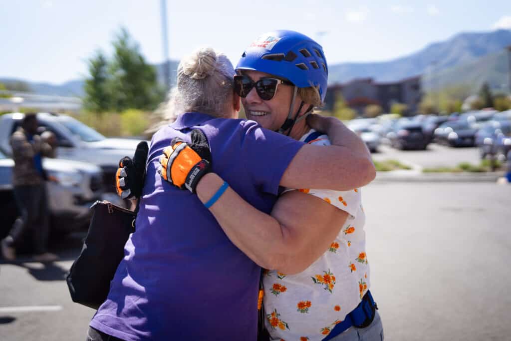Two woman hugging each other after one successfully lands after rappelling down the Residence Inn Building during the 2025 CDCAC Over the Edge fundraiser