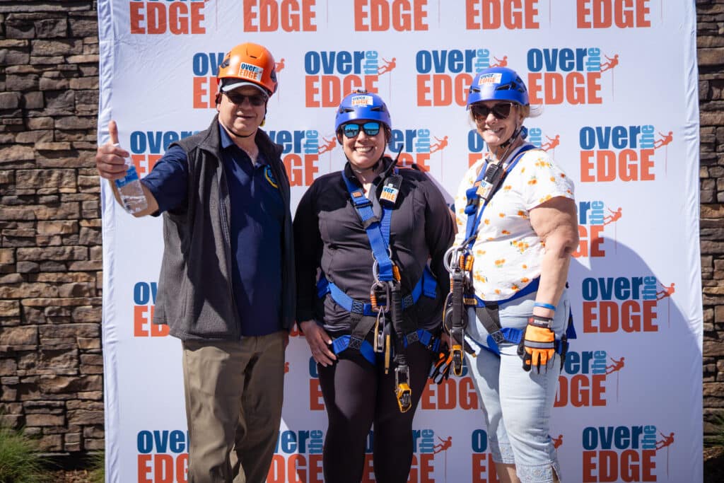 3 adults, one male two females standing in-front of a Over the Edge backdrop