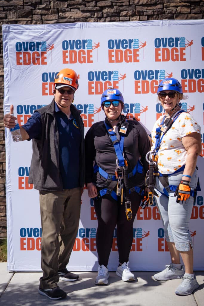 3 adults, one male two females standing in-front of a Over the Edge backdrop