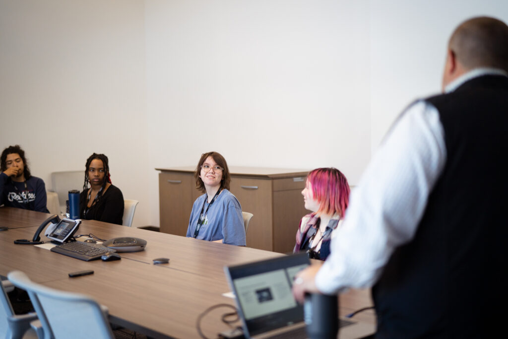 4 young adults at a table watching a male adult do a presentation