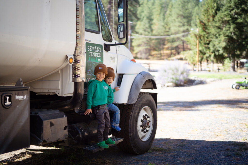 Two young boys sitting on the side of a white utility truck smiling at the camera