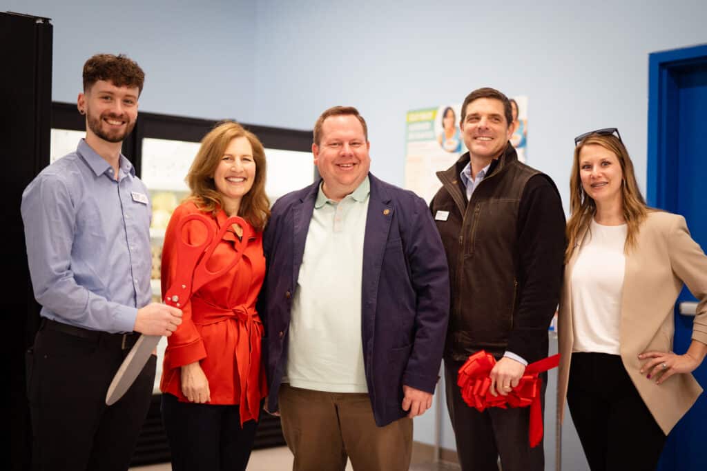 A group of 5 adults smiling at a camera. Man to the left is holding scissors after a ribbon cutting ceremony at CDCAC'S Food Pantry Event