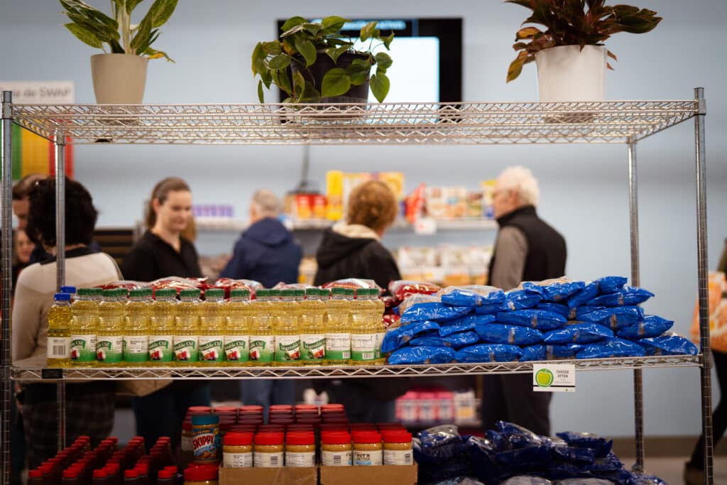 Vegetable oil, pasta, and peanut butter stacked on a metal rack for CDCAC'S Food Pantry