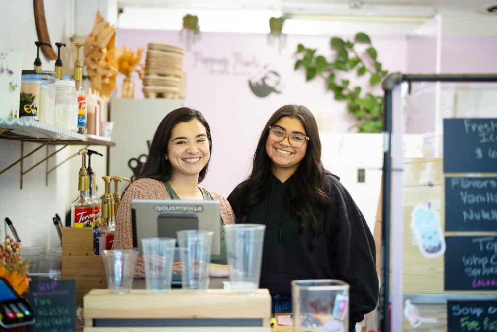 Popping Pearls Boba-8 Two women with brunette hair standing behind a desk smiling at the camera