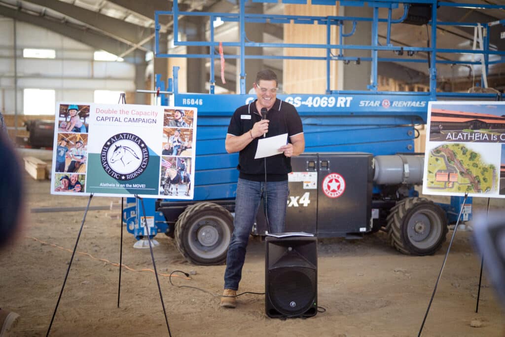 A man wearing a black shirt and dark wash jeans looking at a paper during his presentation