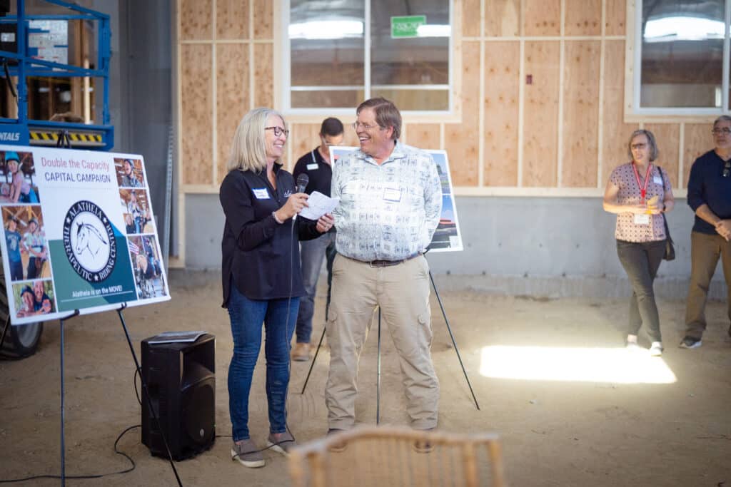 A male and female smiling holding a mic and a piece of paper doing a presentation together