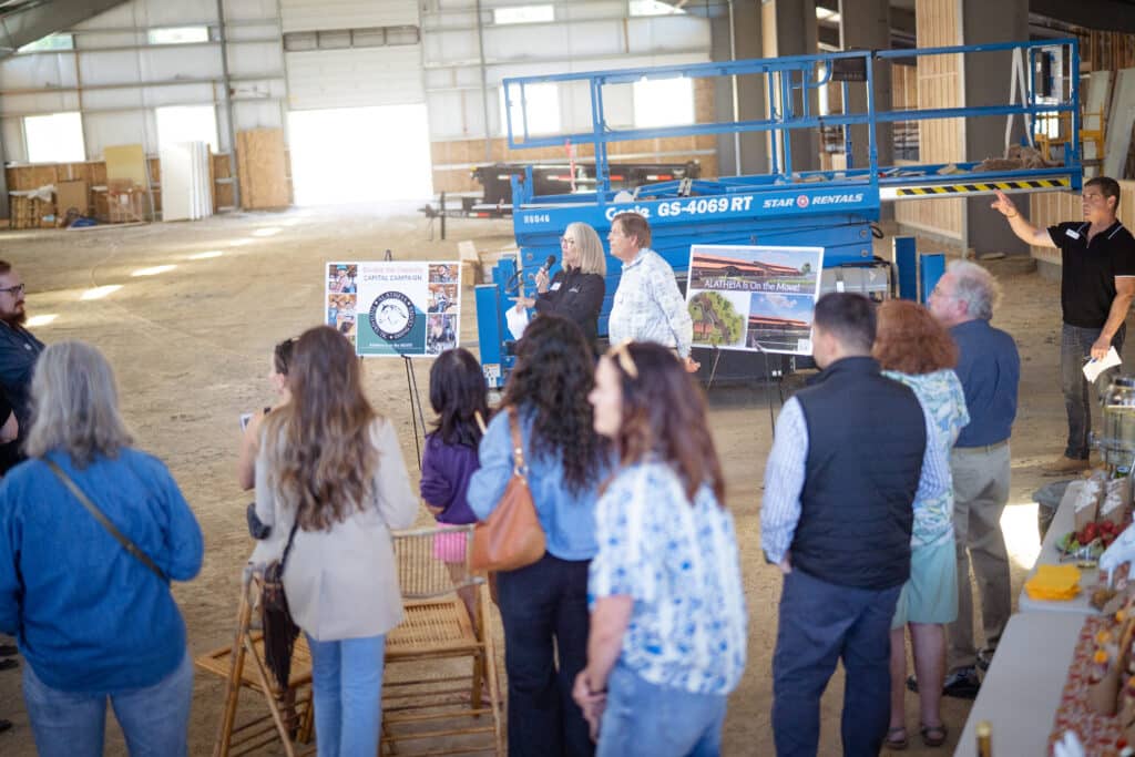 A group of adults watching a male and female present at a horse riding center