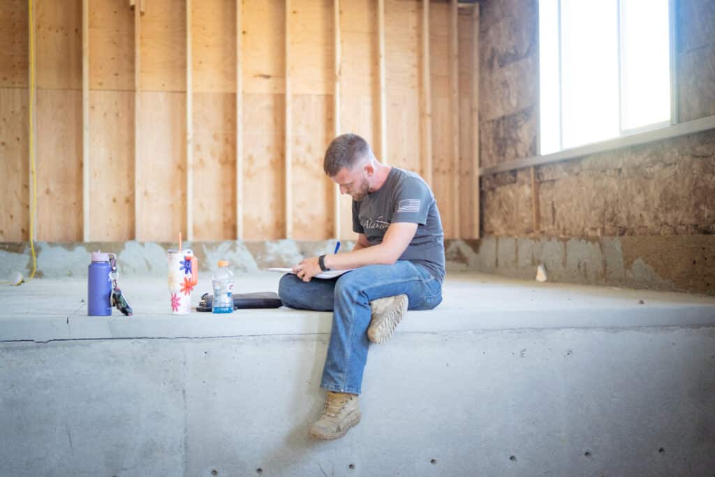 A man sitting on a concrete stand focused while writing on a piece of paper