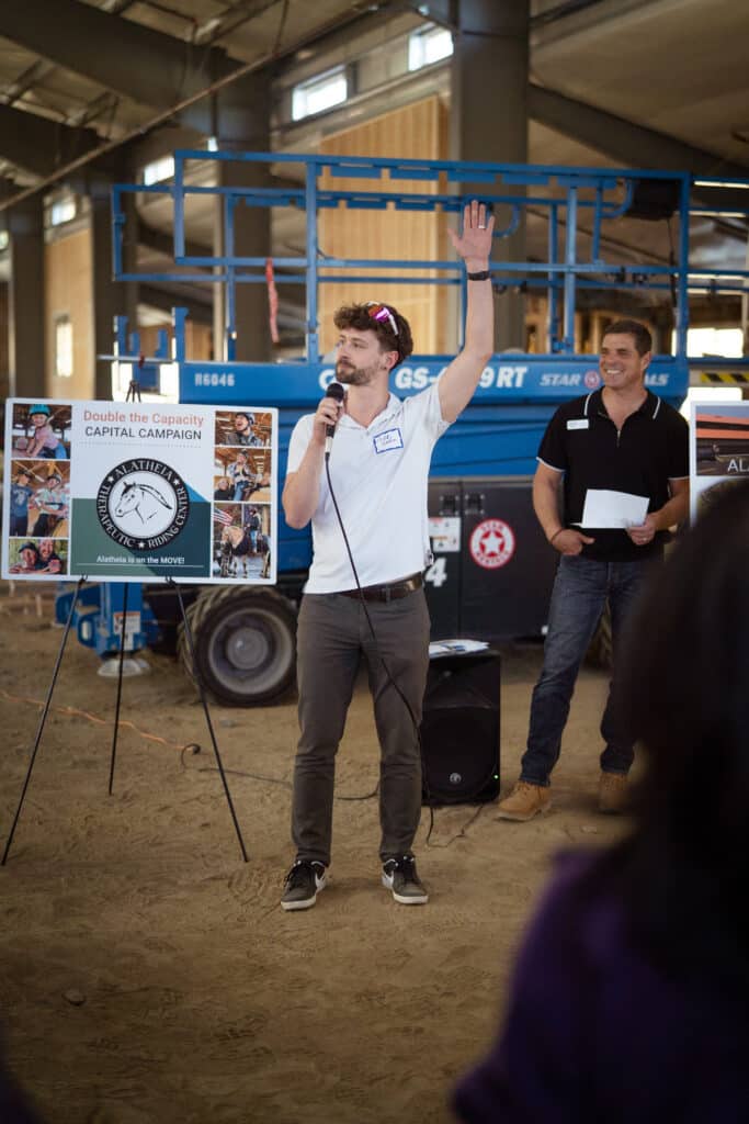 A man with a while collared shirt holding a mic while raising his left hand