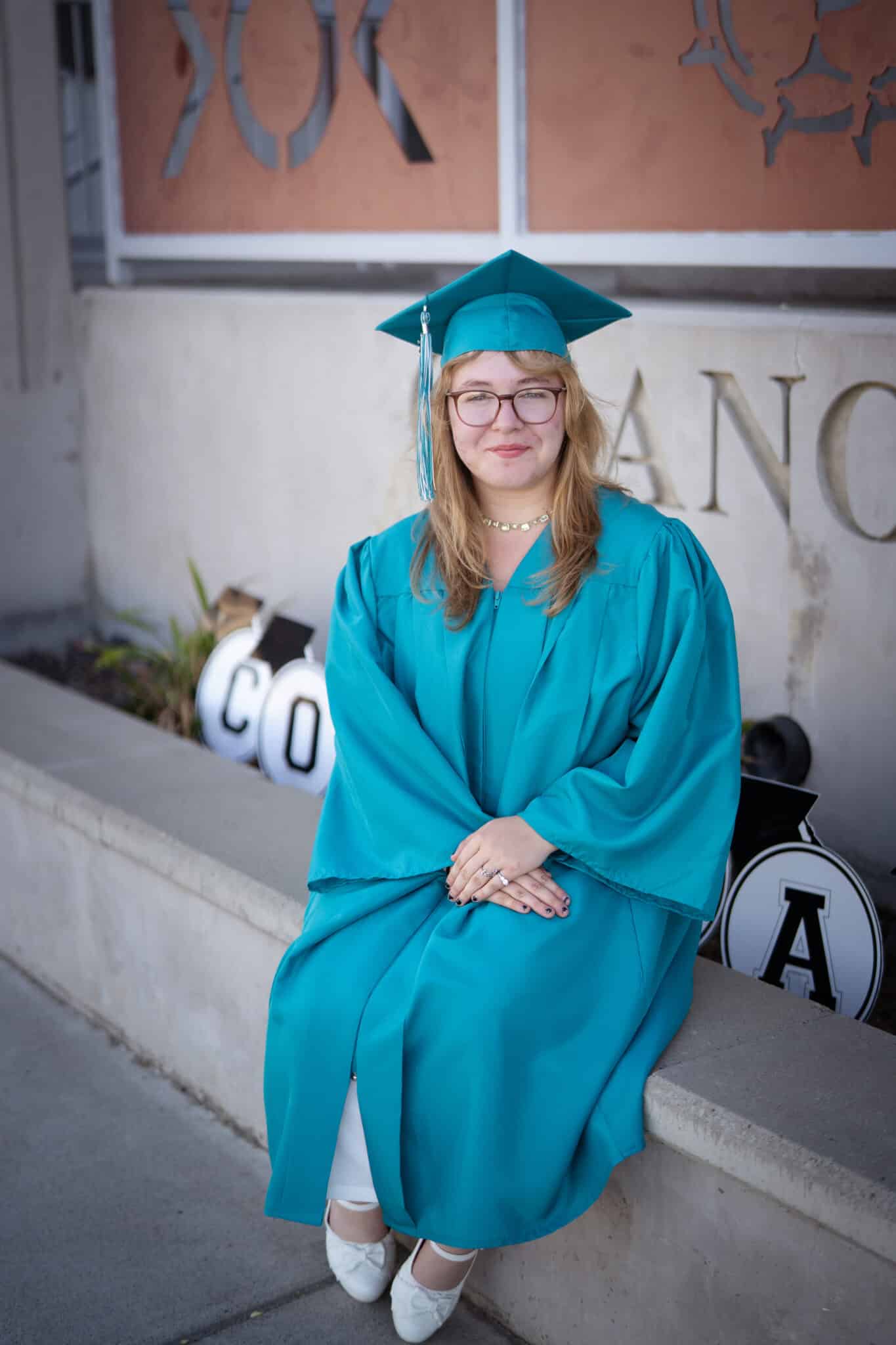Graduate posing for a photo wearing a teal cap and gown.