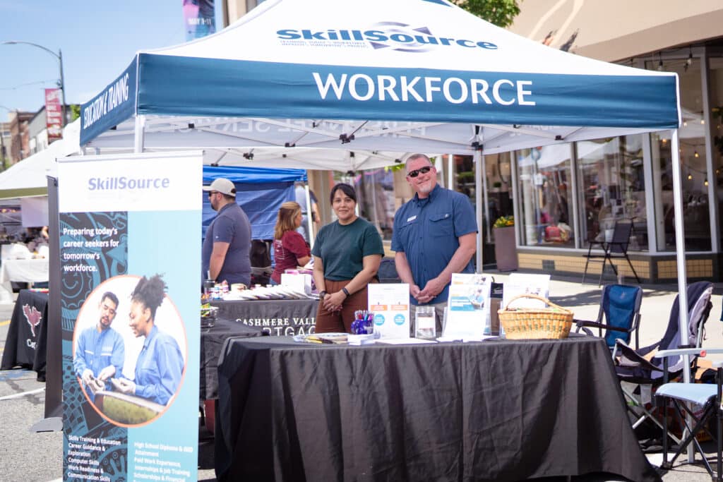 LaTerraza2024-03 Two members of SkillSource staff standing behind an outdoor booth