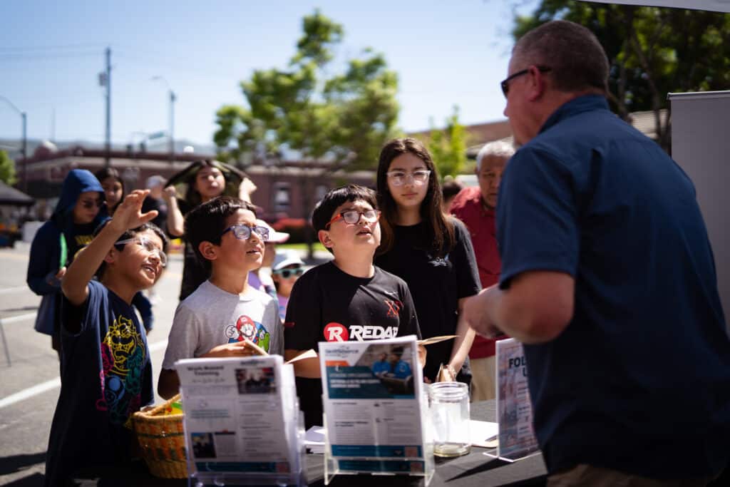 LaTerraza2024-14 A group of children are talking to an adult at an outdoor booth