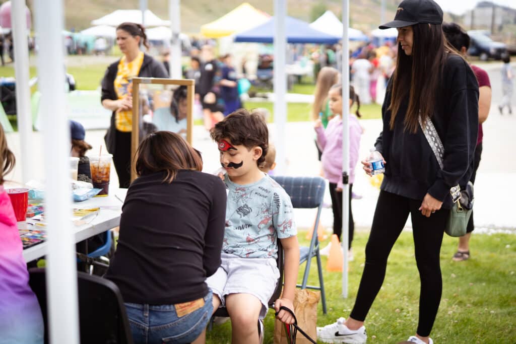A young boy getting his face painted by a volunteer woman