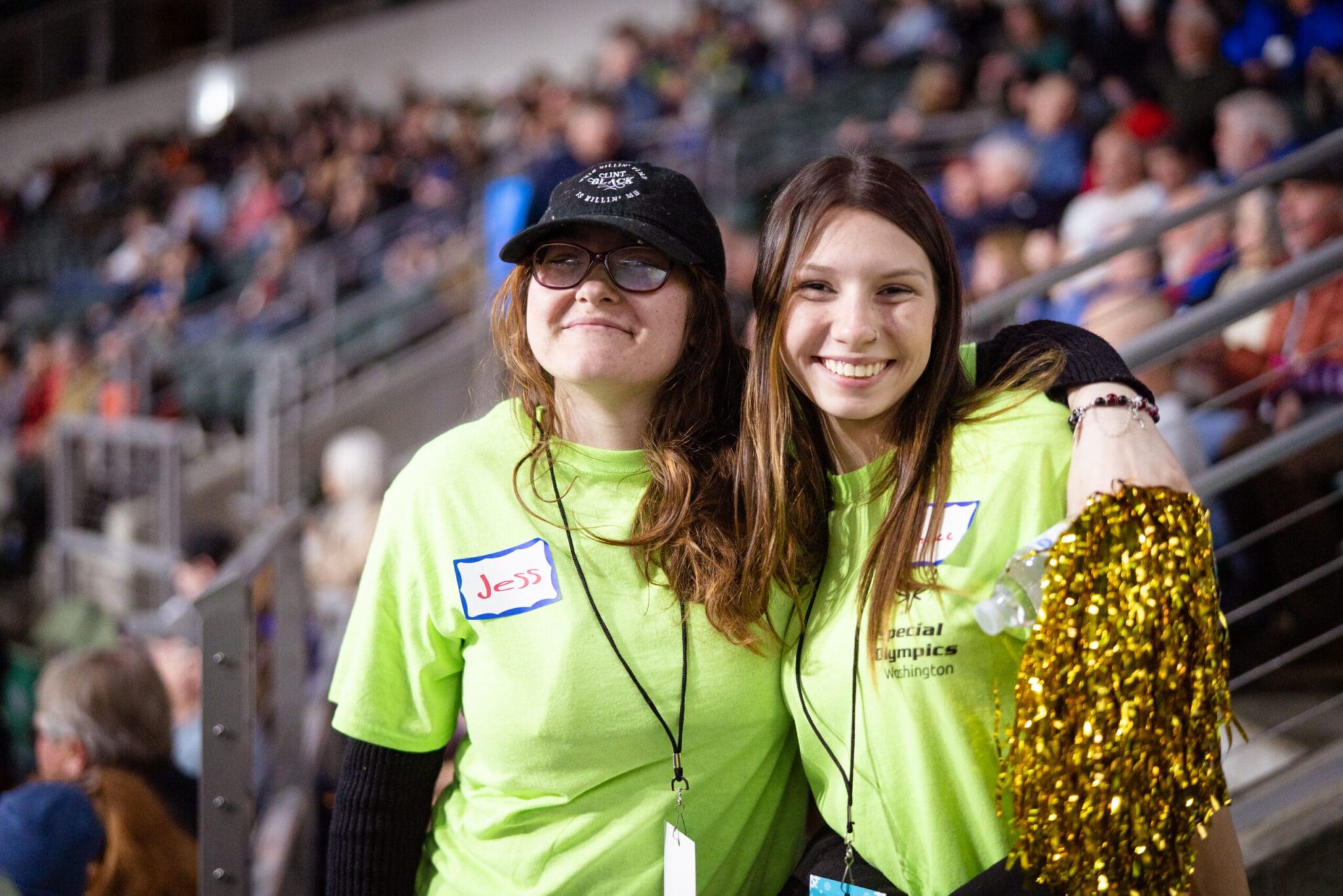Two smiling youth in bright yellow t-shirts hold gold pom poms.