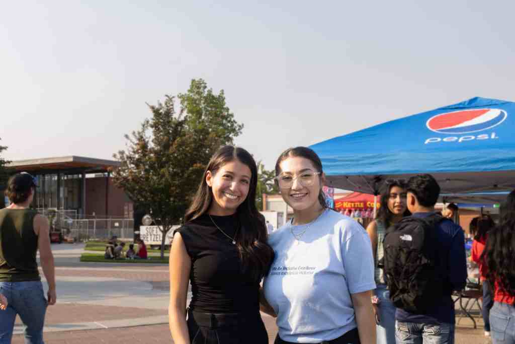 Two brunette women are standing next to each other are smiling at the camera.
