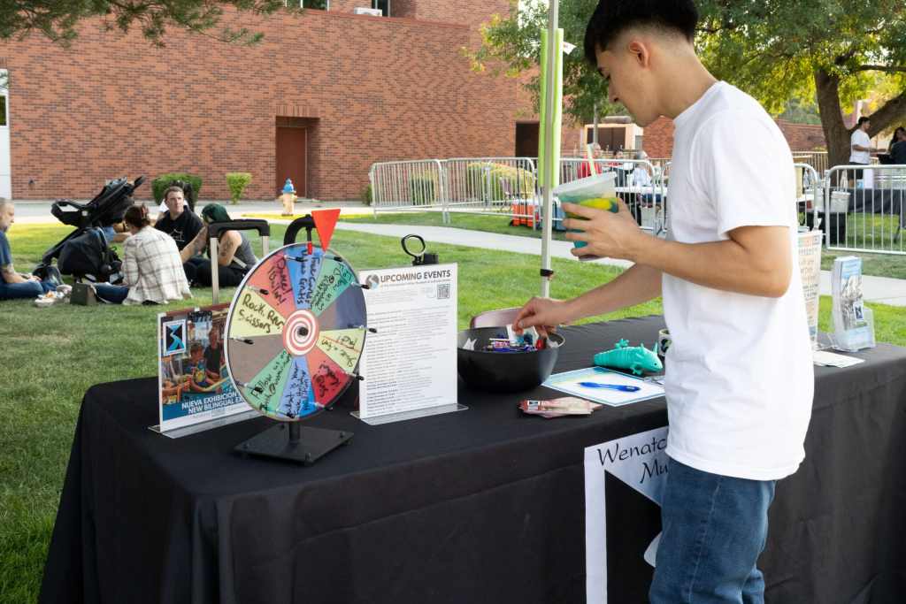 A young male is outdoors holding a drink while looking at a booth with candy and flyers.