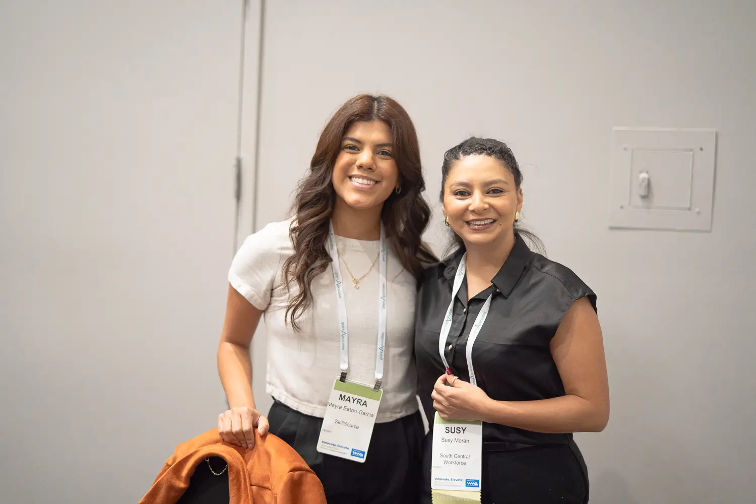 Two dark-haired women wearing conference badges stand shoulder to shoulder.