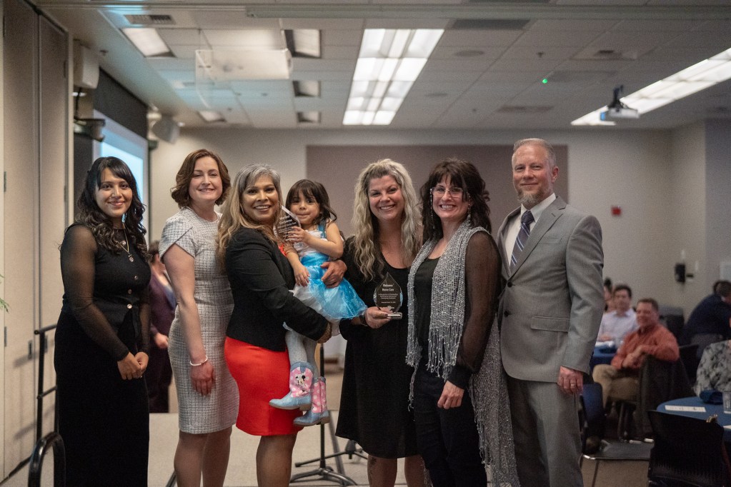 A cluster of nicely dressed people gather for a photo on the edge of a stage.