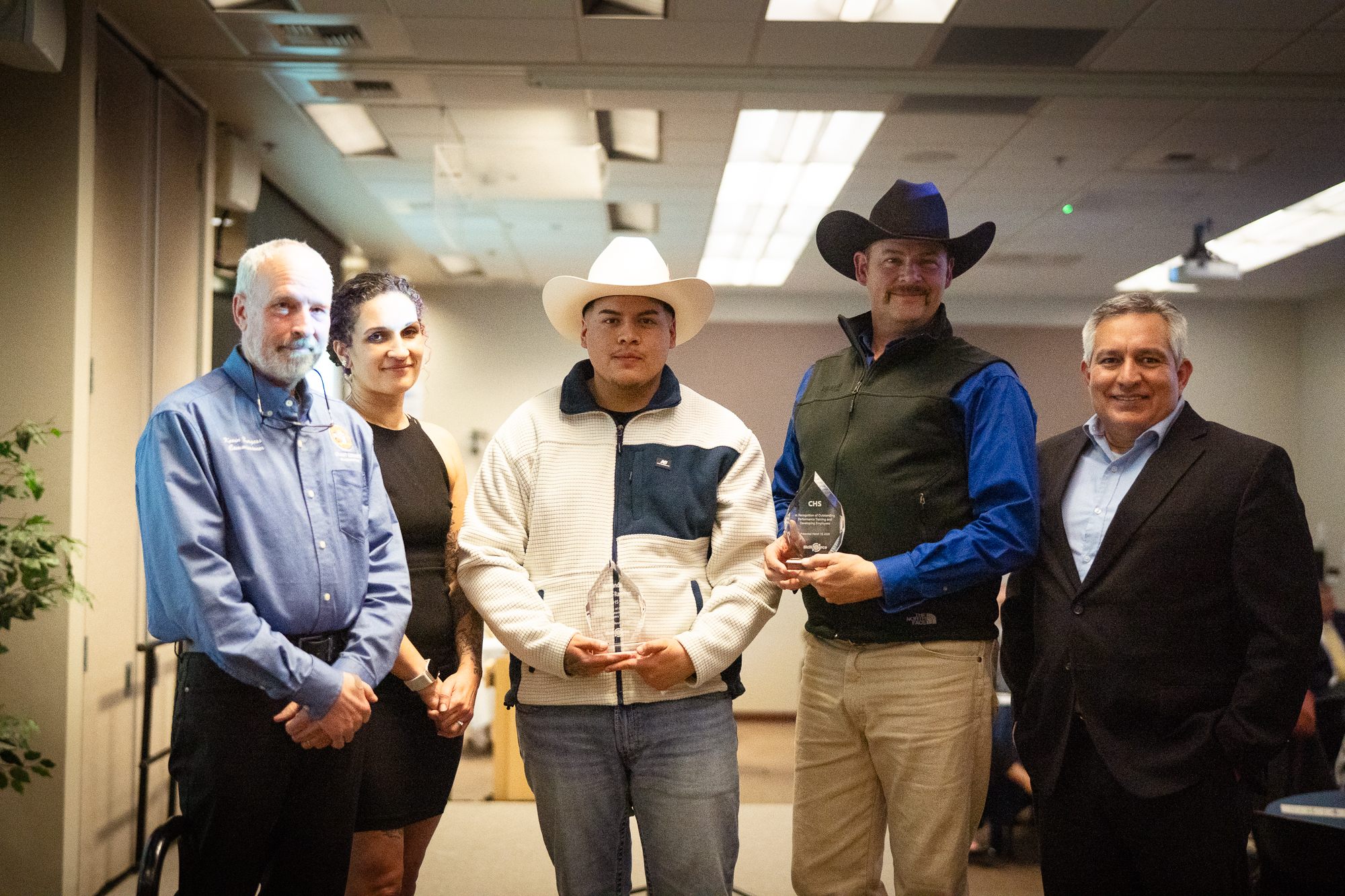 Five men standing indoors at a recognition event, posing together for a photo.