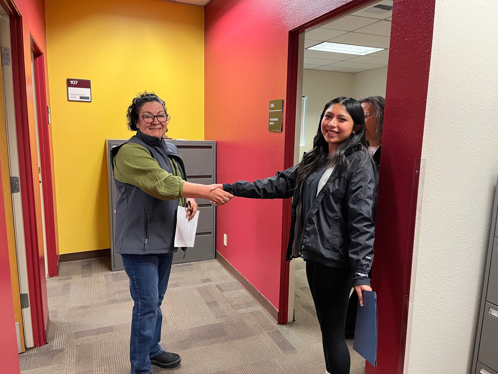 A female instructor with short dark hair shakes the hand of a high school age student.