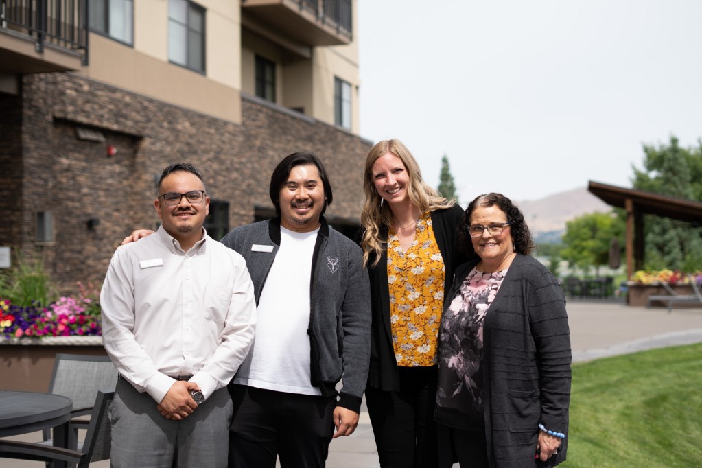 Two men and two women are standing outdoors smiling at a camera.