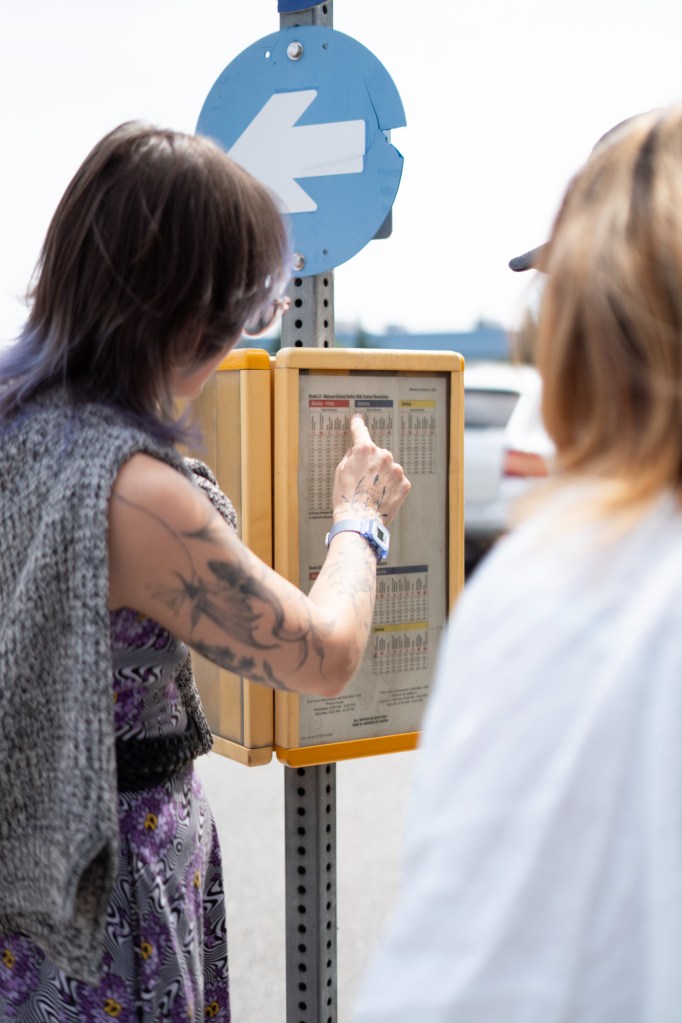 A woman with brown, medium length hair is pointing at a bus stop sign outdoors.